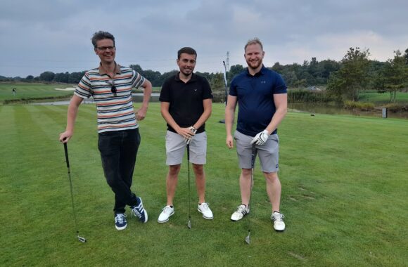 Three members of staff from Look Ahead and AD Construction standing on a golf course with their golf clubs.